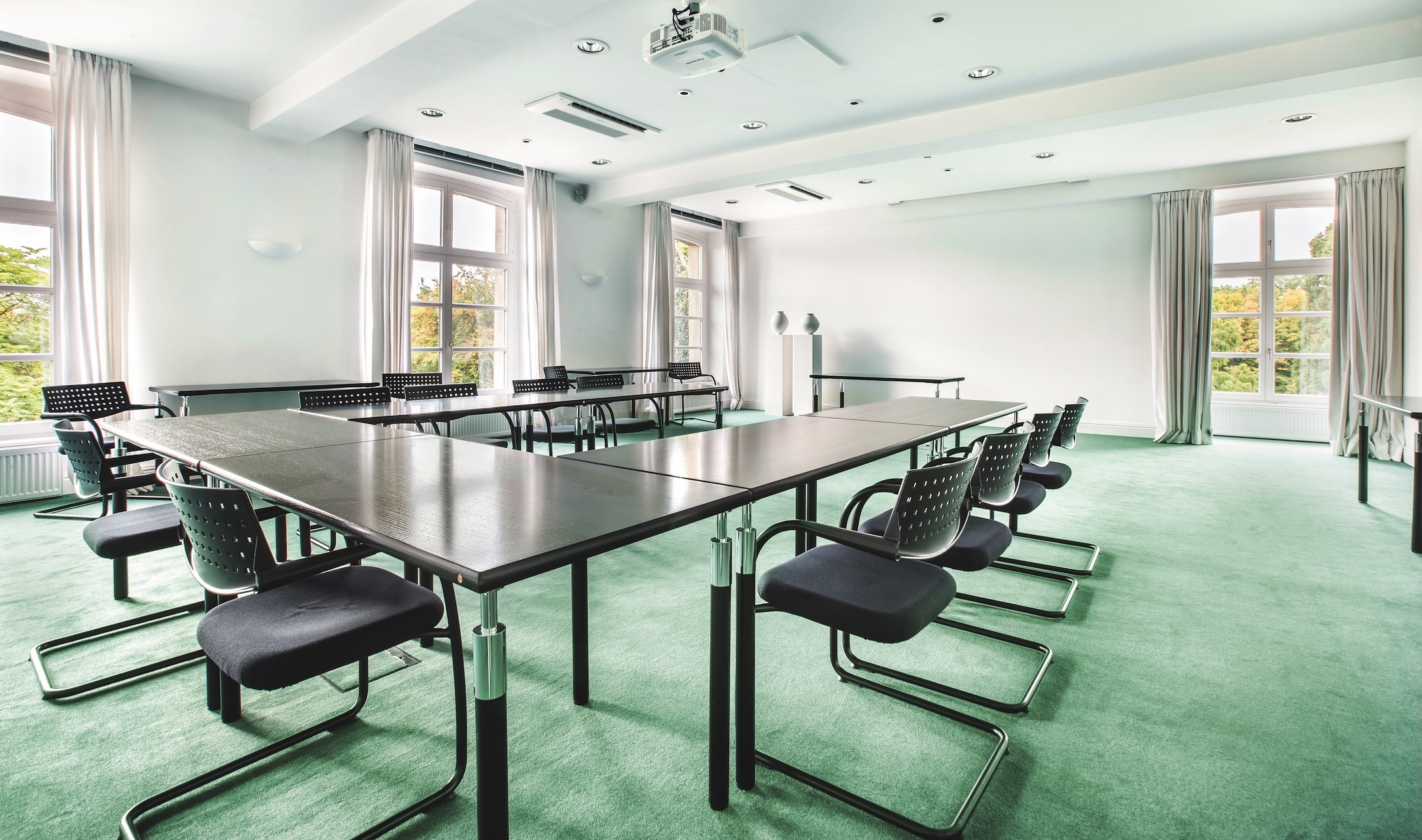 Moderner, lichtdurchfluteter Konferenzraum mit langem Tisch in U-Anordnung und großen Fenstern.