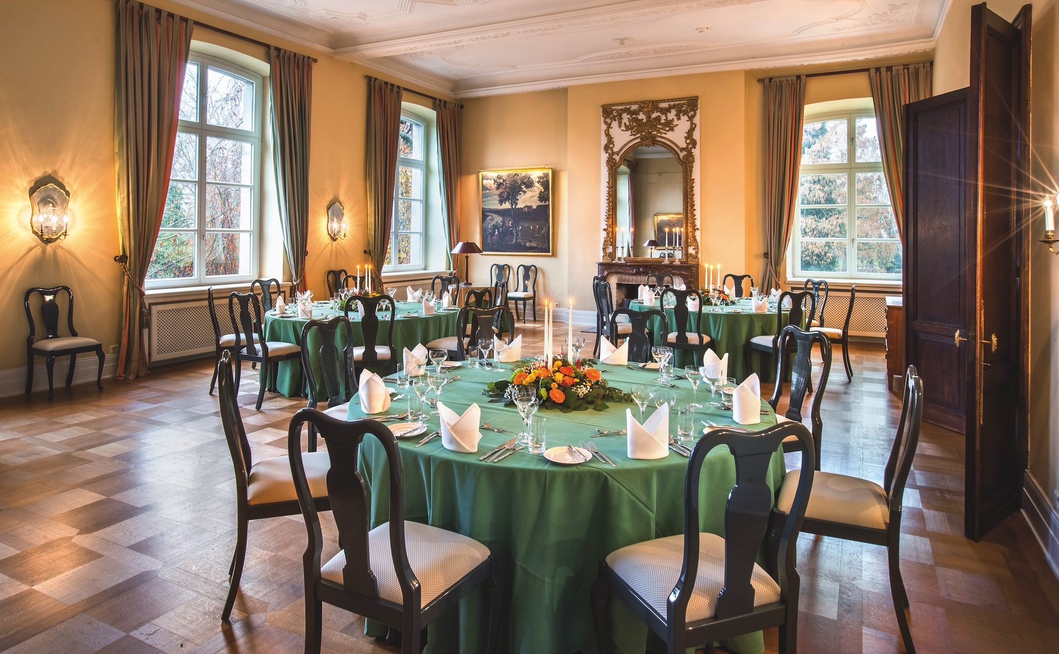 Großer Veranstaltungssaal im Herrenhaus mit gedeckten Tischen für jeweils mehrere Personen, Kerzenlicht und klassischem Ambiente.