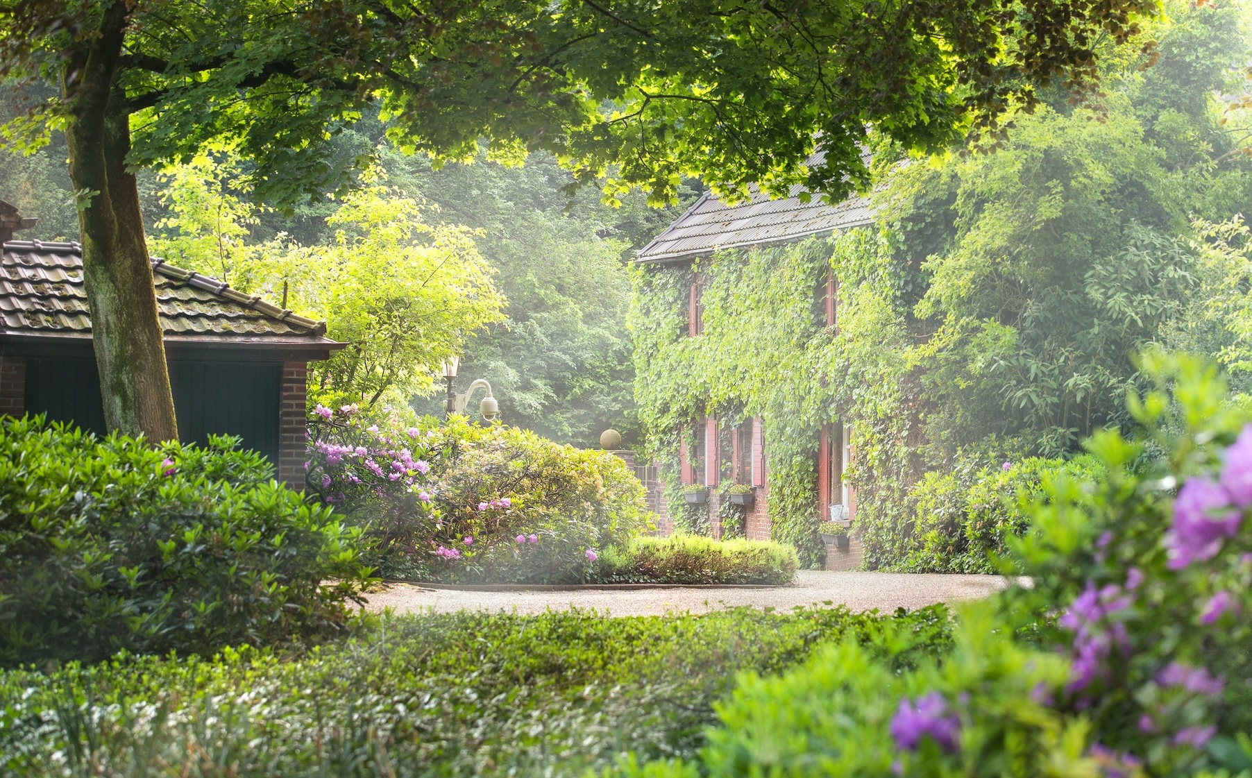 Idyllischer Innenhof mit Backsteingebäude, üppigem Grün und blühenden Pflanzen.